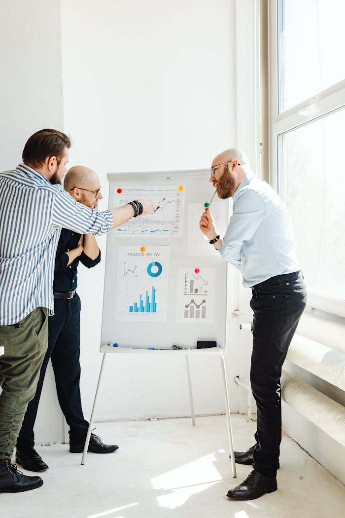 Three business professionals discussing financial charts and reports indoors during the day.